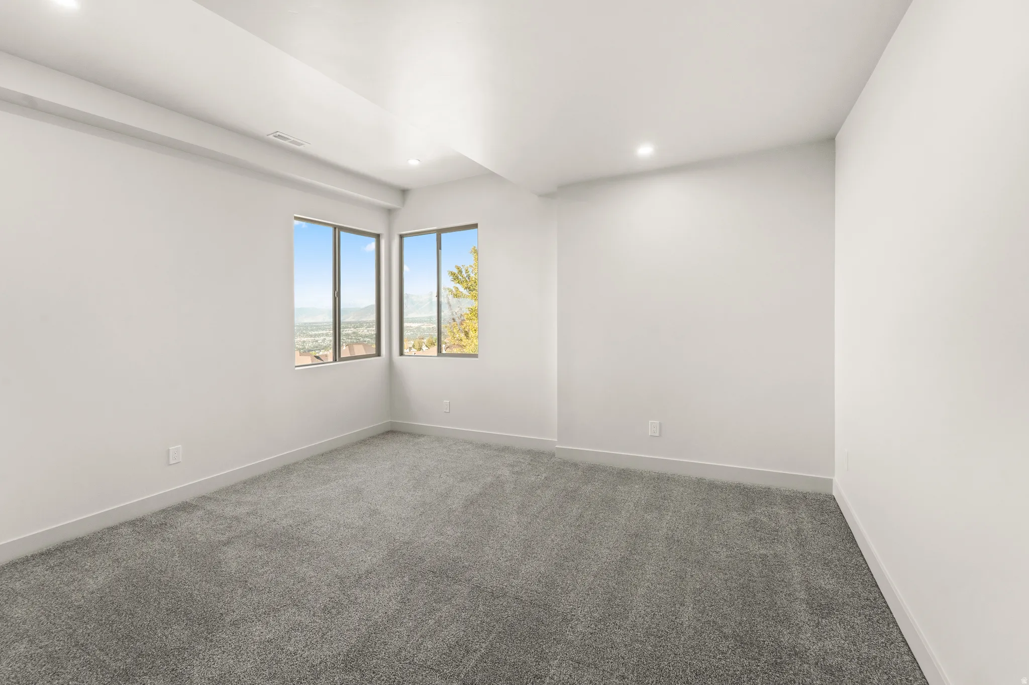 Recessed lighting illuminates the neutral gray carpeting and white painted walls
