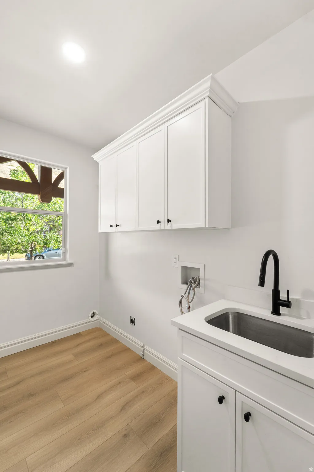 White shaker cabinetry with crown molding, stainless steel sink with matte black faucet, and wood-finish flooring