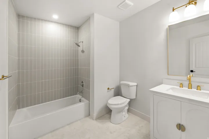 Bathroom featuring a white bathtub, gray vertical tile surround, white vanity with gold hardware, gold-framed mirror, and gold-finish faucet