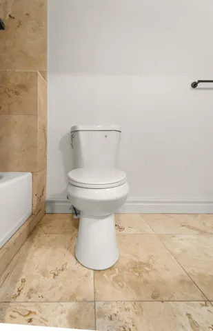White toilet fixture with a two-piece design, complemented by large-format natural stone floor tiles