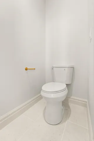 White toilet with a gold-finish toilet paper holder and light-toned tile flooring