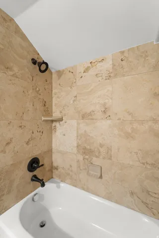 Alcove bathtub featuring a tile surround, built-in shelf, and dark-finish fixtures