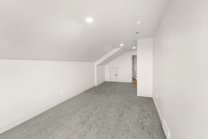 Sloped ceiling room featuring recessed lighting, a door with a black handle, and gray carpet flooring