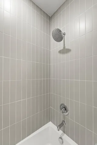 White bathtub with chrome fixtures, a rainfall shower head, and light-colored vertical tile surround