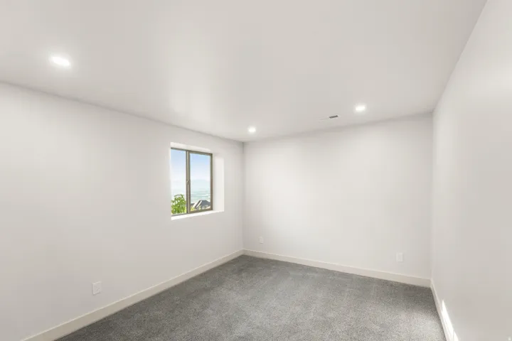 Recessed lighting illuminates this room, featuring light gray carpeting and white walls