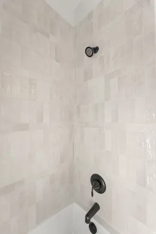 Bathtub shower combination with matte black fixtures and light-toned, rectangular wall tiles