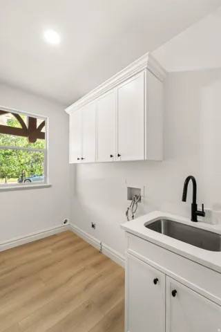 White shaker cabinetry with crown molding, stainless steel sink with matte black faucet, and wood-finish flooring