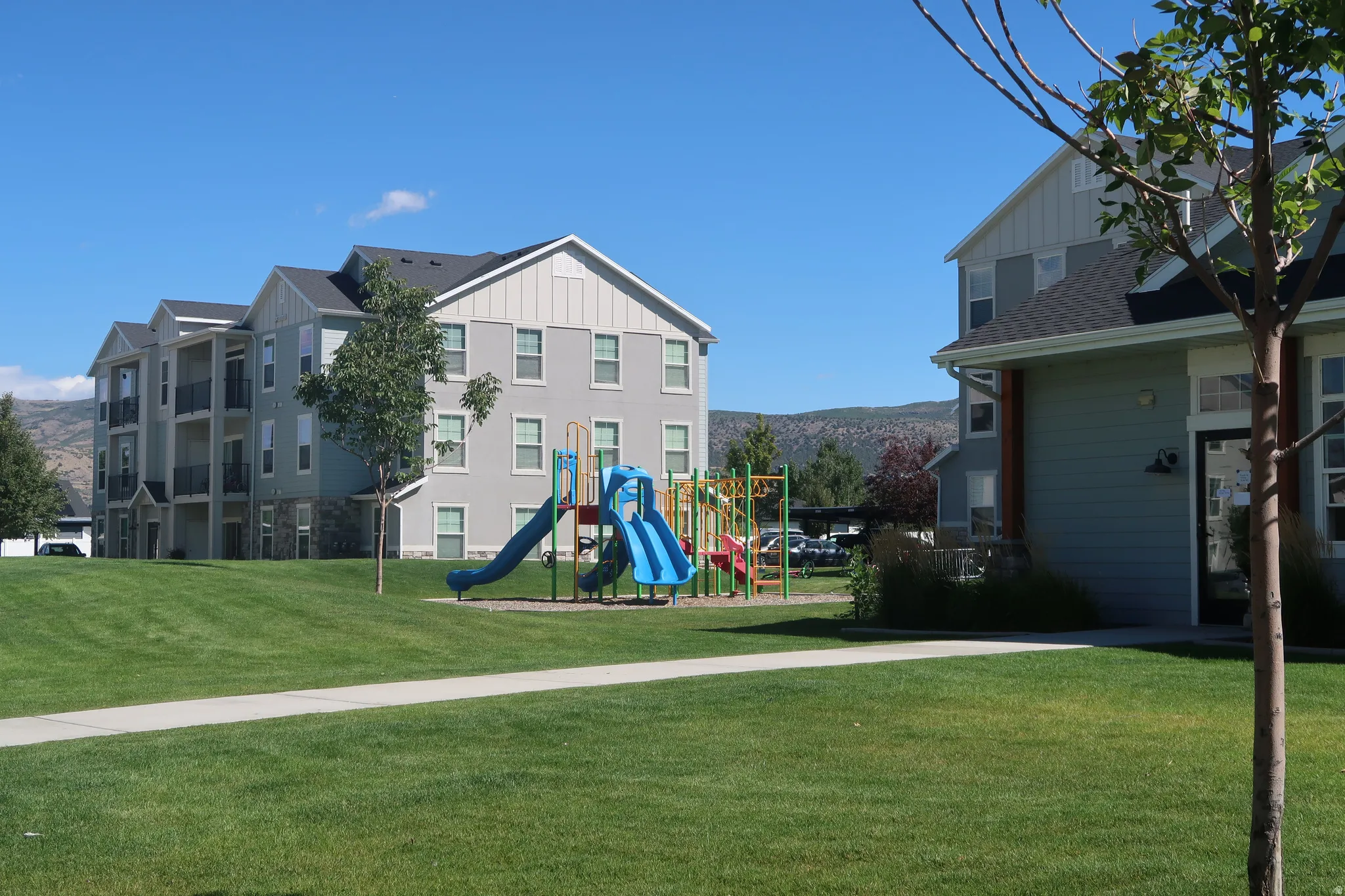 Expansive green space featuring a built-in playground, mature trees, and a paved walkway
