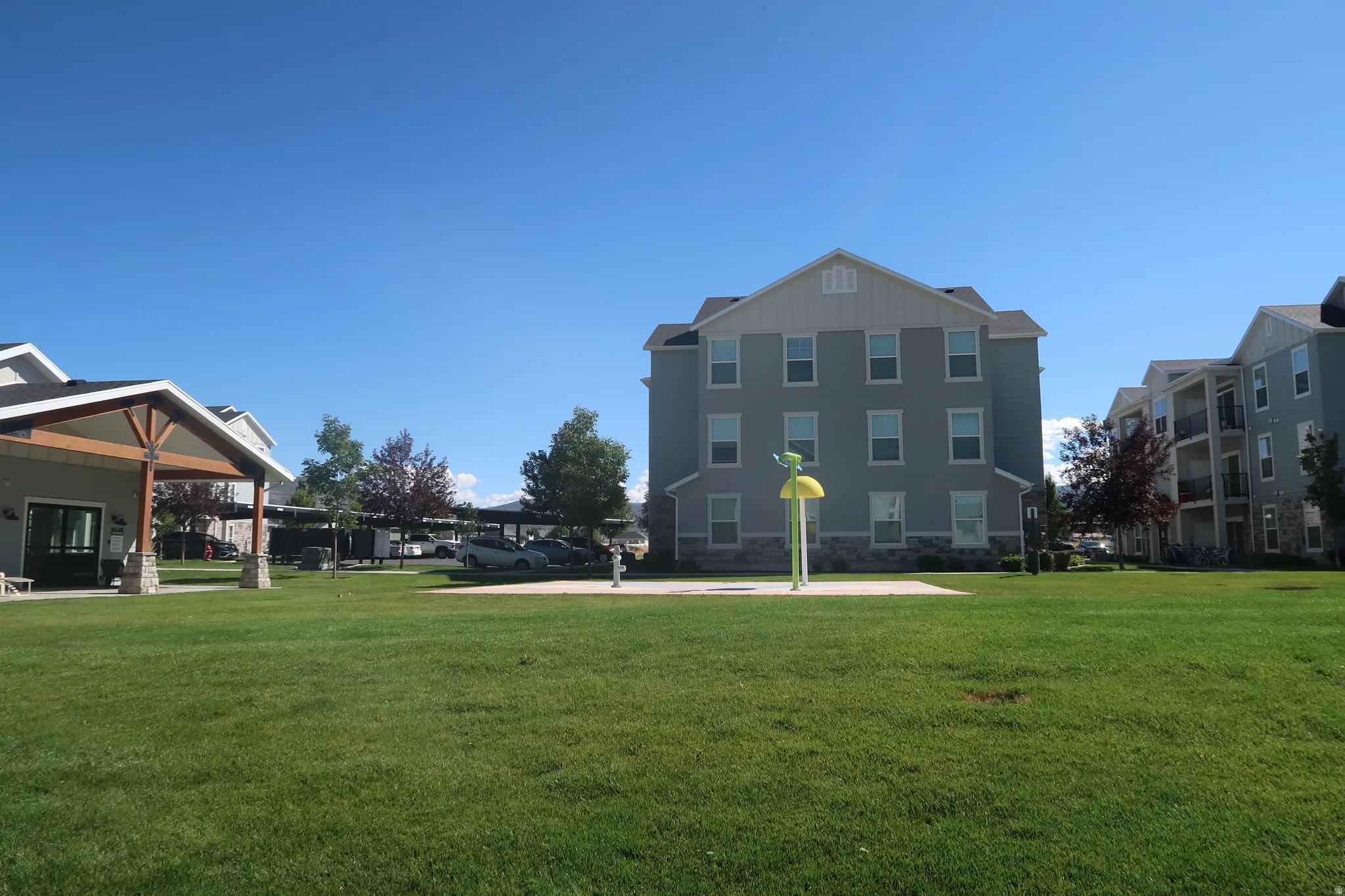 Expansive green space featuring a splash pad, covered parking, and multi-story buildings with balconies