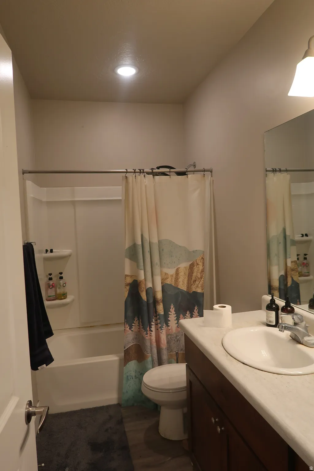 White bathtub with integrated shelving, dark wood-finish vanity with white countertop, integrated sink, and wall-mounted mirror