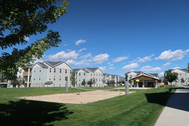 Spacious green lawn featuring a sand volleyball court and a pavilion with seating