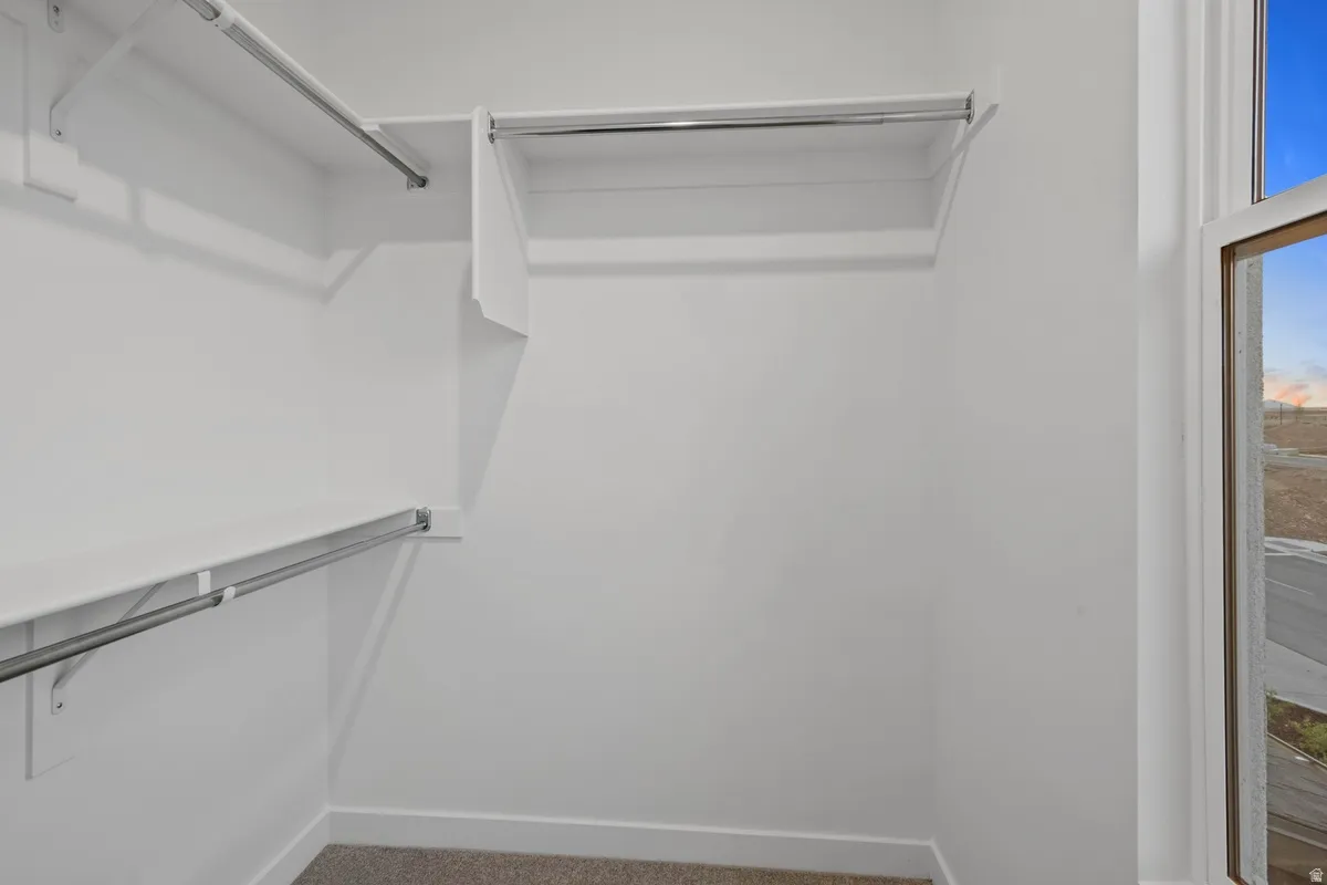 Walk-in closet featuring white shelving, multiple hanging rods, and an exterior window