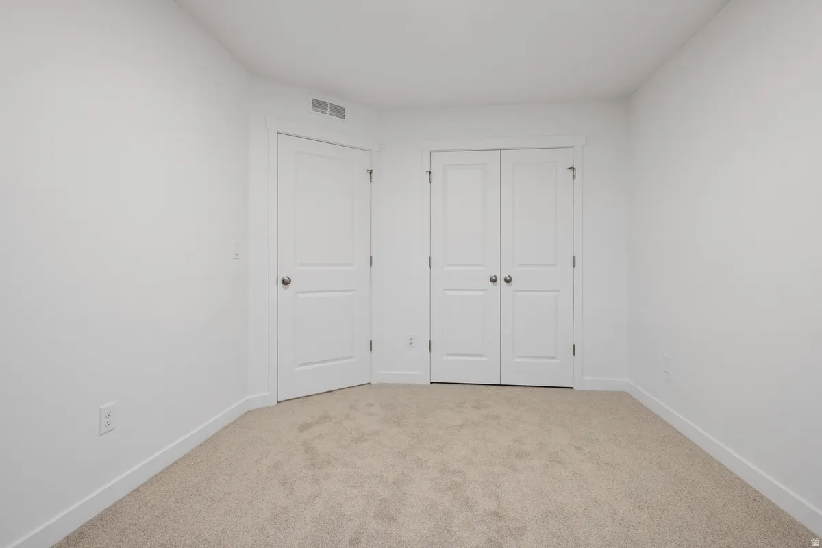 White walls with light-colored carpeting, featuring a single panel door and a set of bi-fold doors