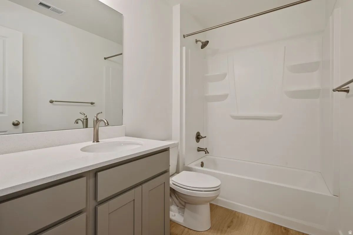 Full bathroom featuring a white tub/shower combination, light wood-finish flooring, a vanity with a white countertop and undermount sink, and brushed nickel fixtures