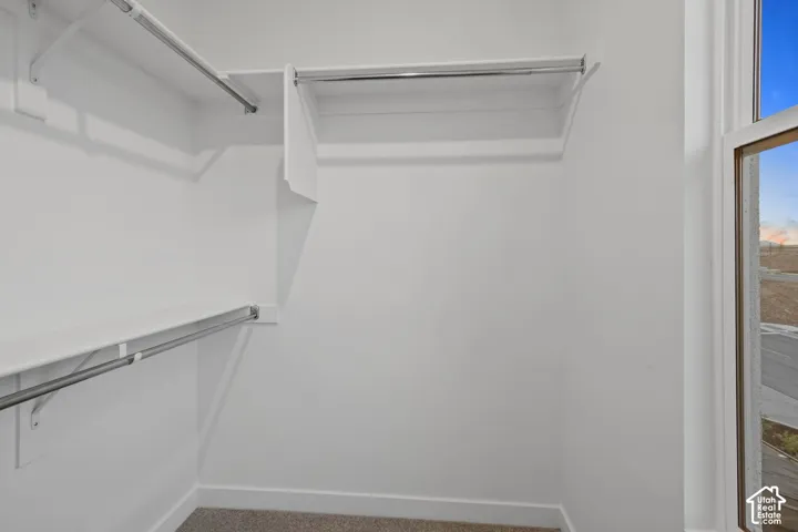 Walk-in closet featuring white shelving, multiple hanging rods, and an exterior window