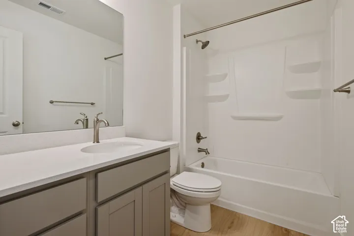 Full bathroom featuring a white tub/shower combination, light wood-finish flooring, a vanity with a white countertop and undermount sink, and brushed nickel fixtures