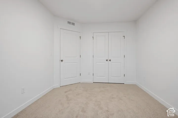 White walls with light-colored carpeting, featuring a single panel door and a set of bi-fold doors