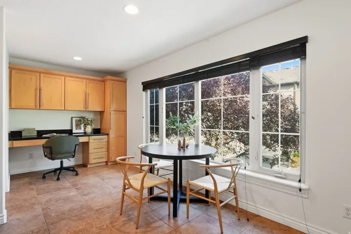 Built-in desk with a dark countertop and ample cabinetry, integrated shelving, and large window with vertical blinds, recessed lighting, and tile flooring