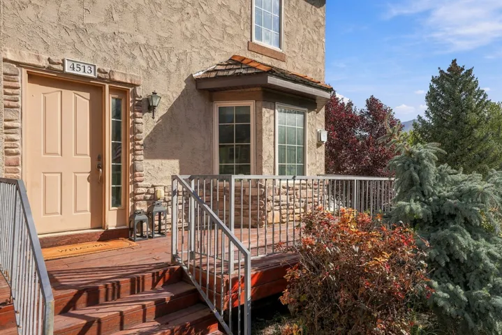 Stucco exterior with stone accents, wood deck entry, bay window with shingle roof, and established landscaping