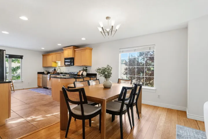 Open-concept living space with wood-finish flooring, a contemporary chandelier, and a kitchen featuring wood cabinetry, stainless steel appliances, and dark countertops