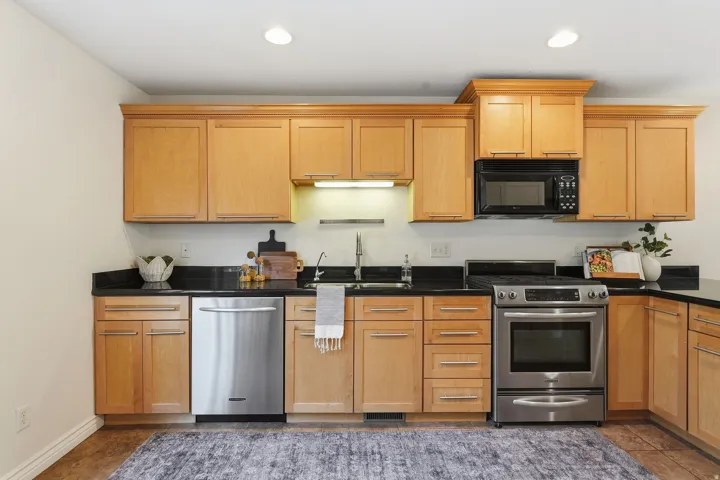 Light wood cabinetry, dark countertops, stainless steel appliances, and wood-finish flooring