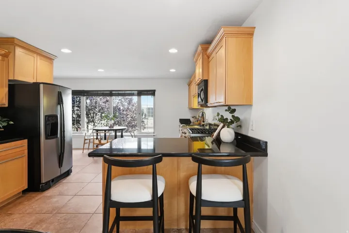 Spacious kitchen featuring wood cabinetry, black countertops, stainless steel refrigerator, and recessed lighting