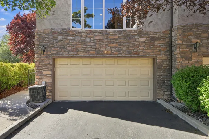 Stone facade with a panel garage door, upper-level windows, and exterior lighting fixtures