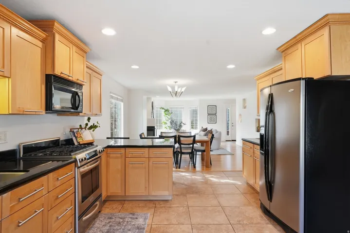 Kitchen featuring light wood-finish cabinetry, dark countertops, stainless steel appliances, and tiled flooring