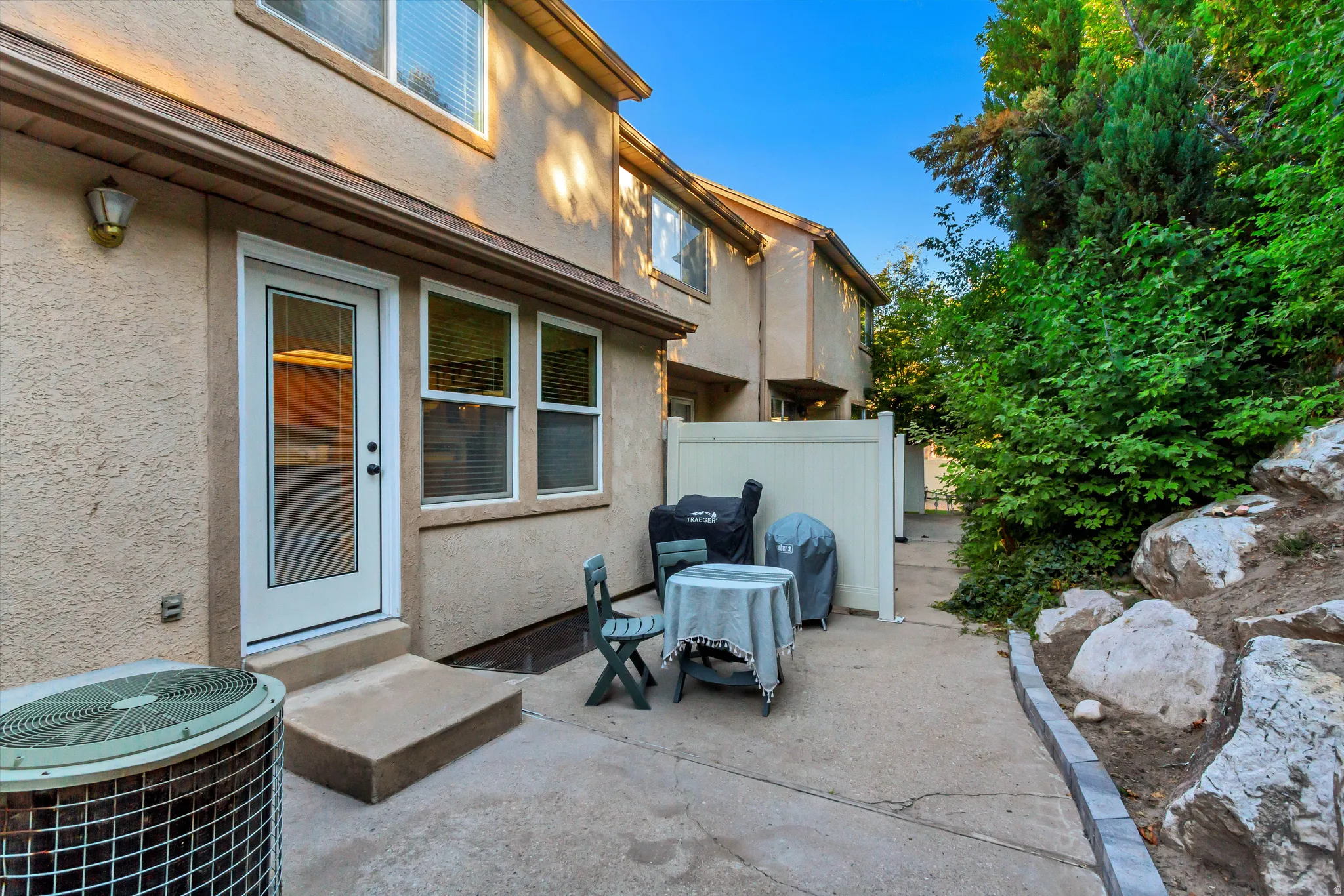 Concrete patio with a privacy fence, stucco exterior, and mature landscaping