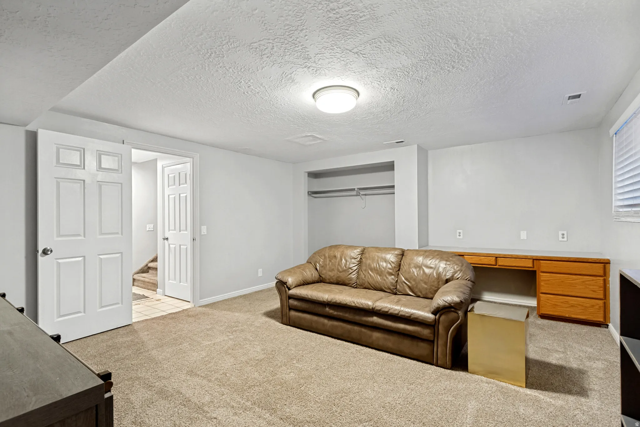 Carpeted room with built-in wood-finish desk, recessed closet space, and window with blinds