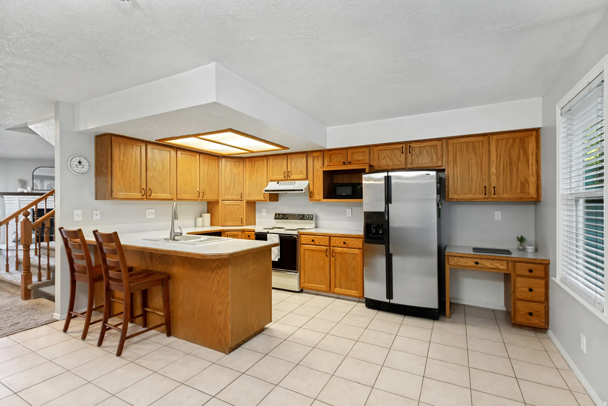 Kitchen featuring wood-finish cabinetry, stainless steel appliances, a built-in desk, and tiled flooring
