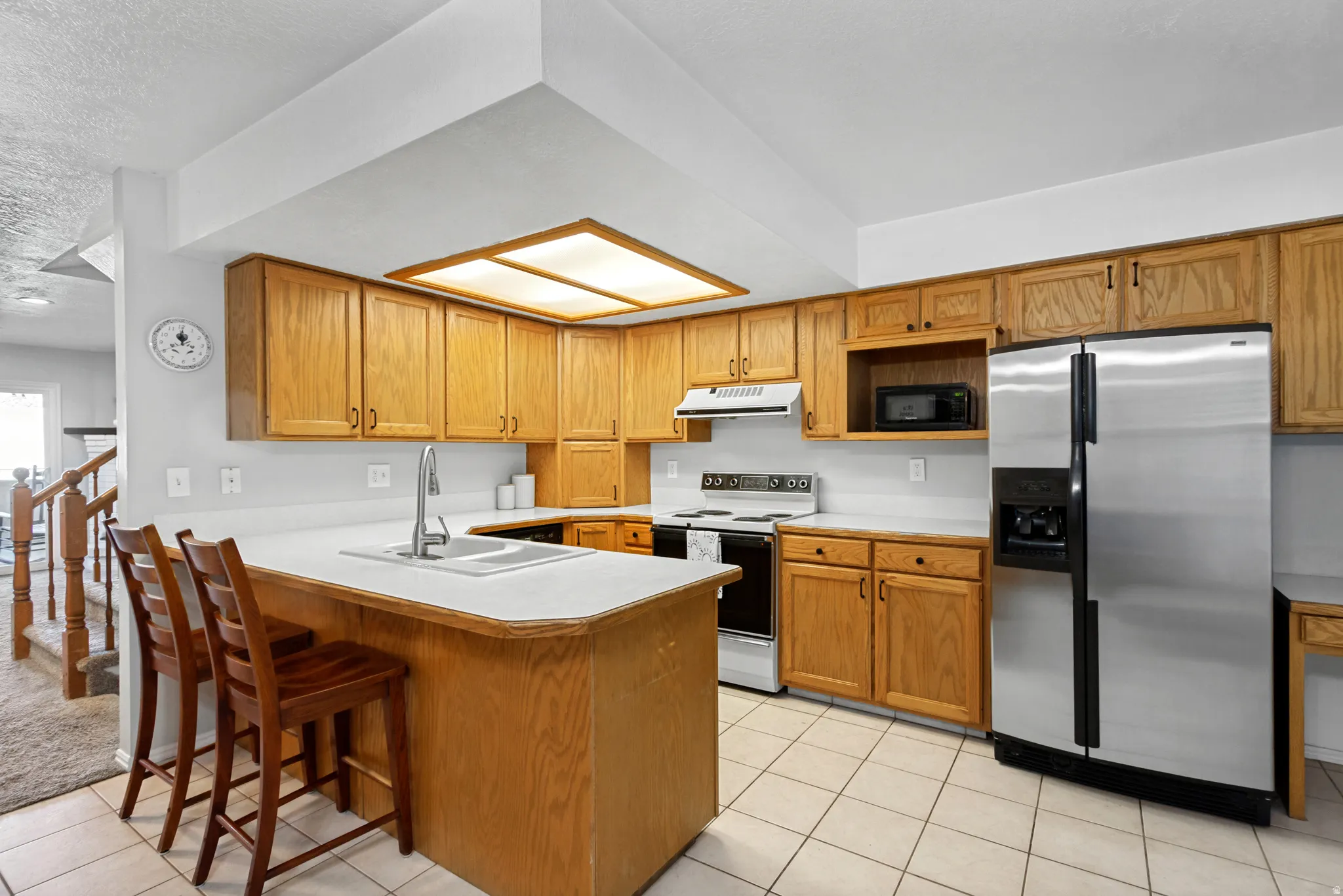 Kitchen featuring wood-finish cabinetry, white countertops, tile flooring, stainless steel refrigerator, and a recessed ceiling light fixture
