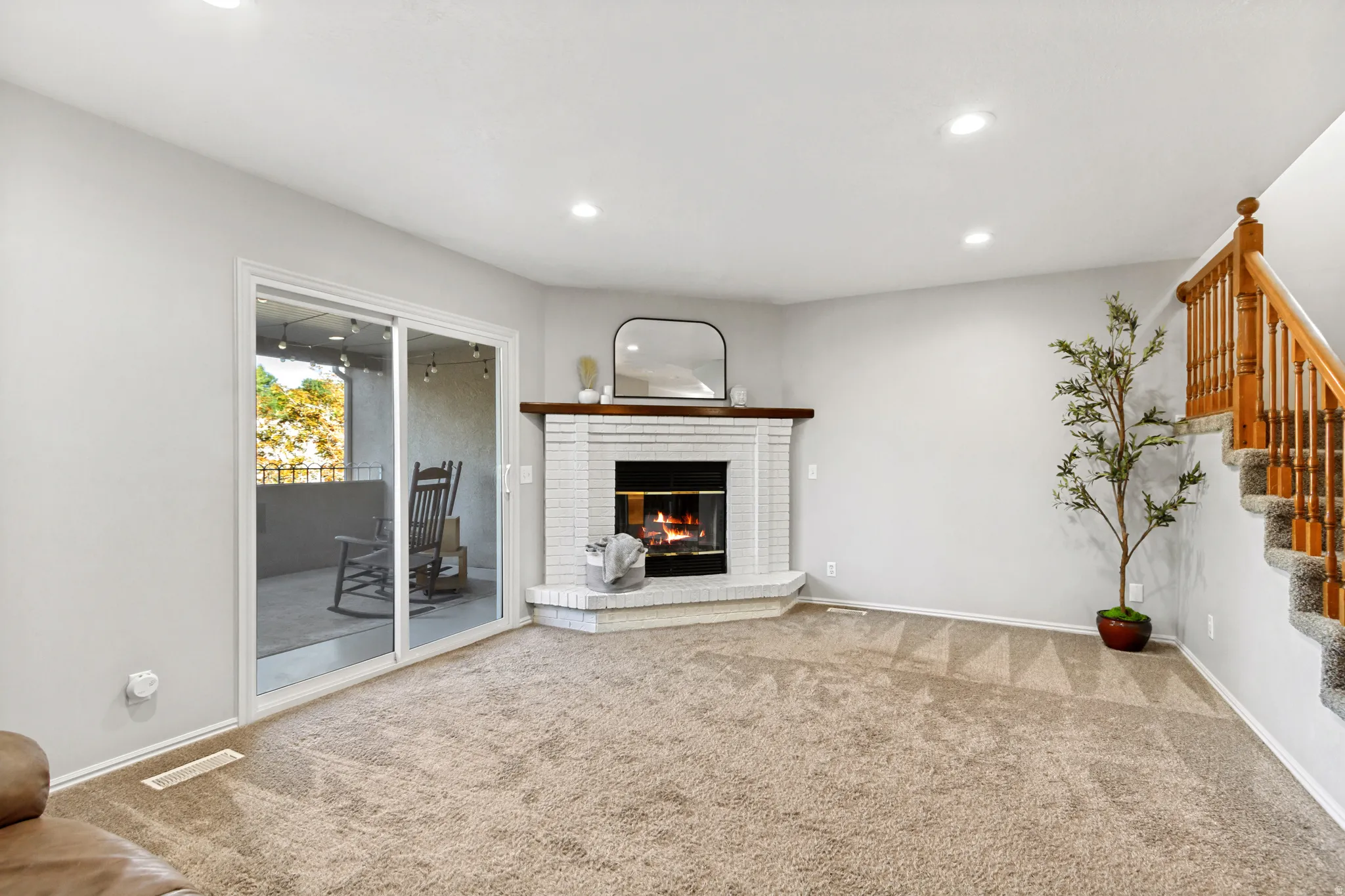Corner-set brick fireplace with a wood mantle, sliding glass door, recessed lighting, and carpeted flooring