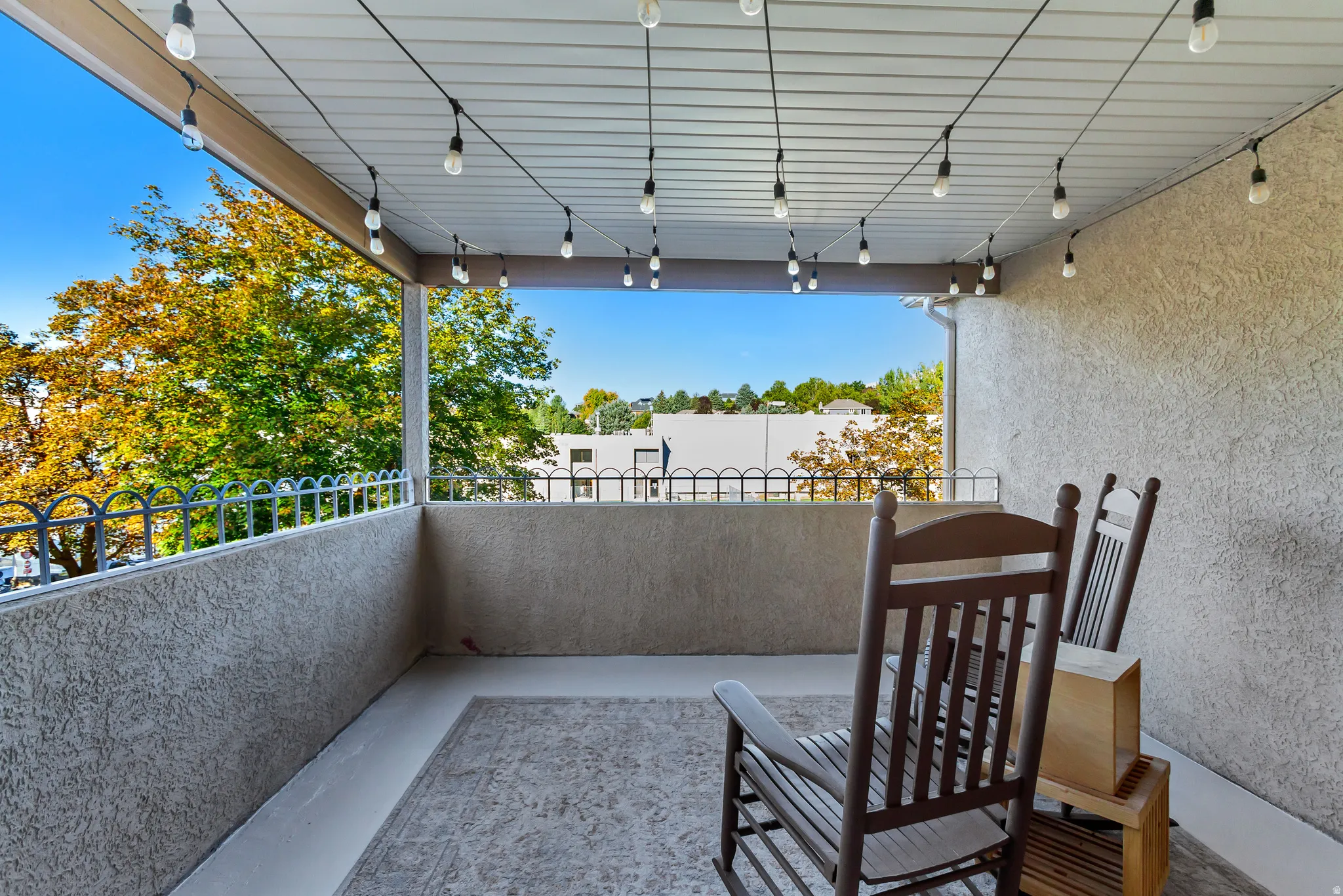 Covered balcony featuring stucco walls, a decorative metal railing, a beadboard ceiling, and string lighting