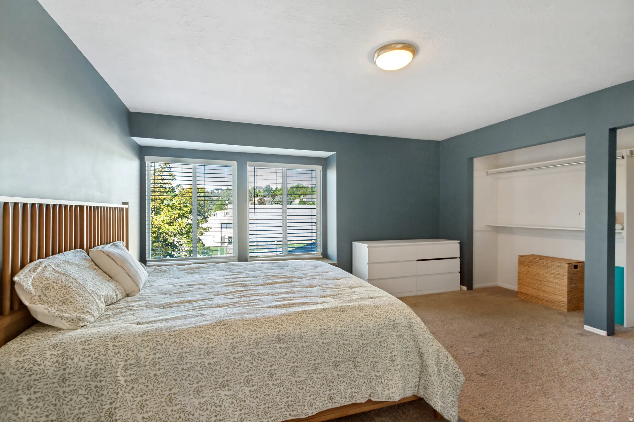 Recessed window bay with white blinds, wall-to-wall carpeting, built-in open closet with shelving and hanging rod, and a flush mount ceiling light fixture