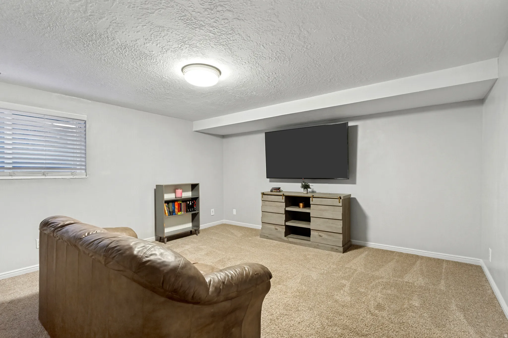 Recessed window with blinds, overhead flush mount lighting, wall-mounted display, and carpeted flooring
