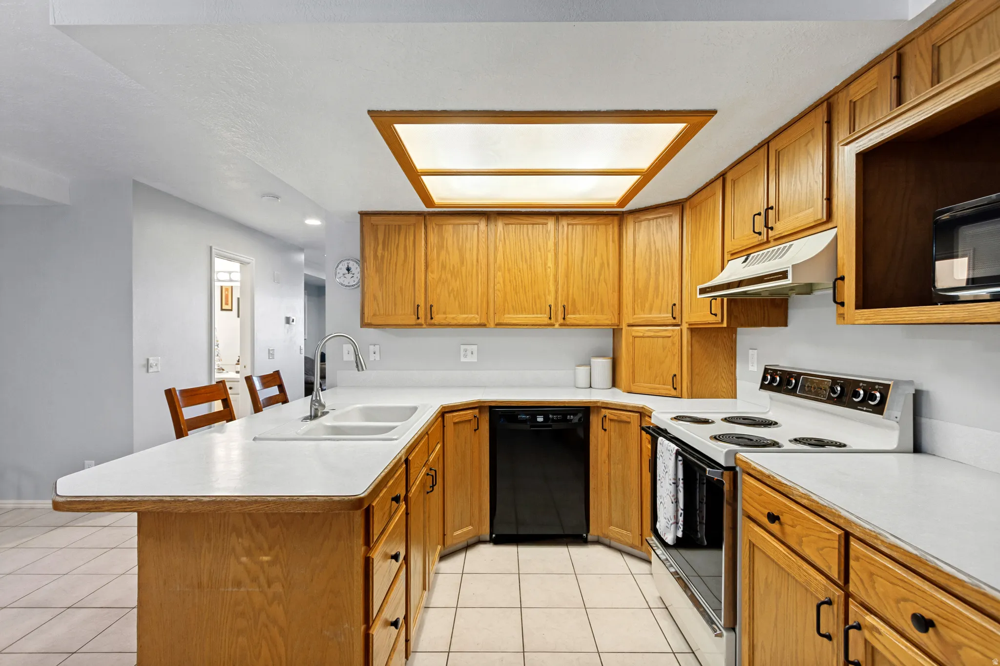 U-shaped kitchen featuring wood cabinetry, white countertops, dual basin sink with a high-arc faucet, and tile flooring