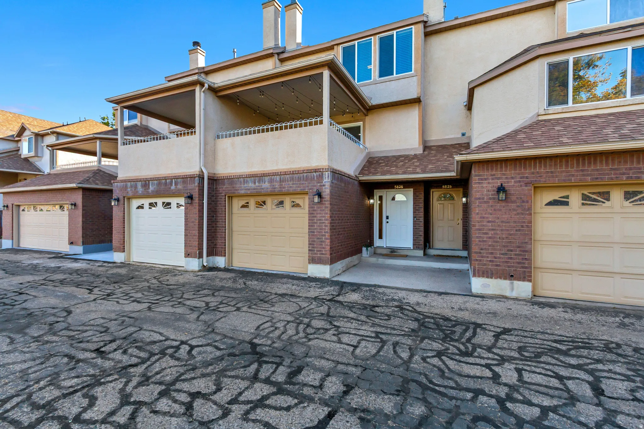 Brick facade with stucco accents, multiple garage entries, second-story balcony, and dual entry doors
