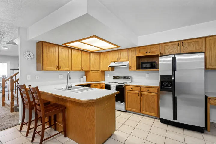 Kitchen featuring wood-finish cabinetry, white countertops, tile flooring, stainless steel refrigerator, and a recessed ceiling light fixture