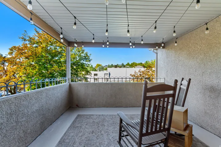 Covered balcony featuring stucco walls, a decorative metal railing, a beadboard ceiling, and string lighting