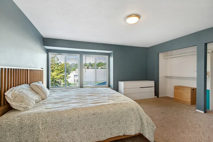 Recessed window bay with white blinds, wall-to-wall carpeting, built-in open closet with shelving and hanging rod, and a flush mount ceiling light fixture