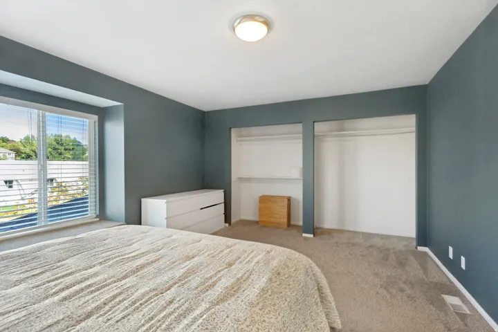 Carpeted room with a large window, integrated window blinds, and dual open closet spaces
