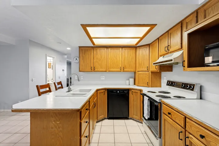 U-shaped kitchen featuring wood cabinetry, white countertops, dual basin sink with a high-arc faucet, and tile flooring