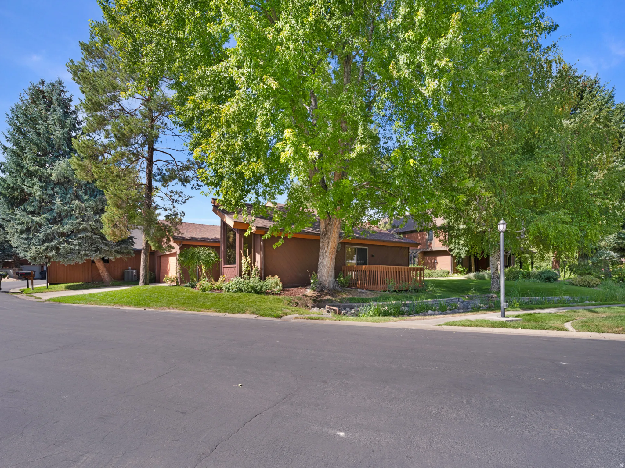 Contemporary exterior with multiple mature trees, a wood-finish deck, and surrounding greenery
