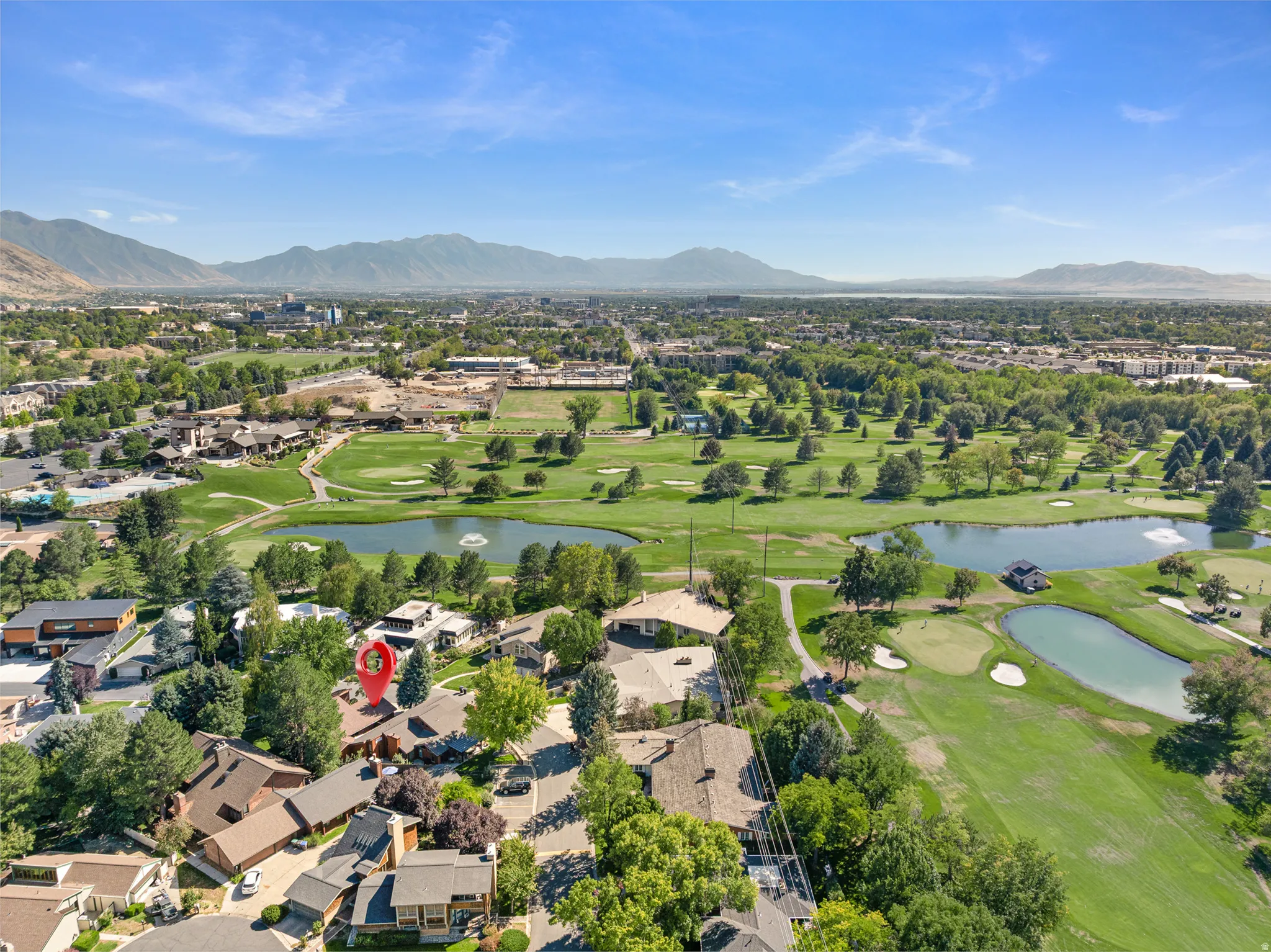 Expansive golf course setting with multiple water features, surrounded by mature trees and mountain scenery