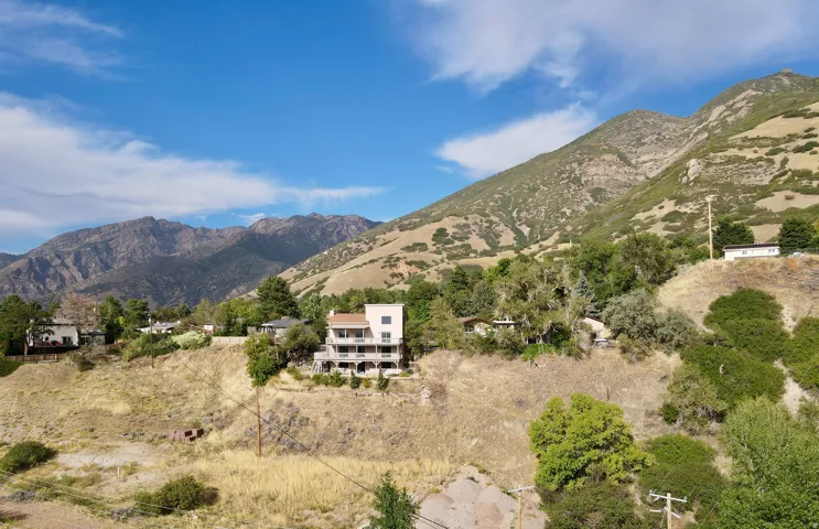 Multi-level residence with balconies, surrounded by natural hillside and mature trees, set against a mountainous backdrop