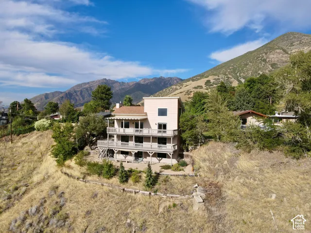 Multi-level dwelling with multiple balconies, a light-colored stucco exterior, and a prominent mountain backdrop
