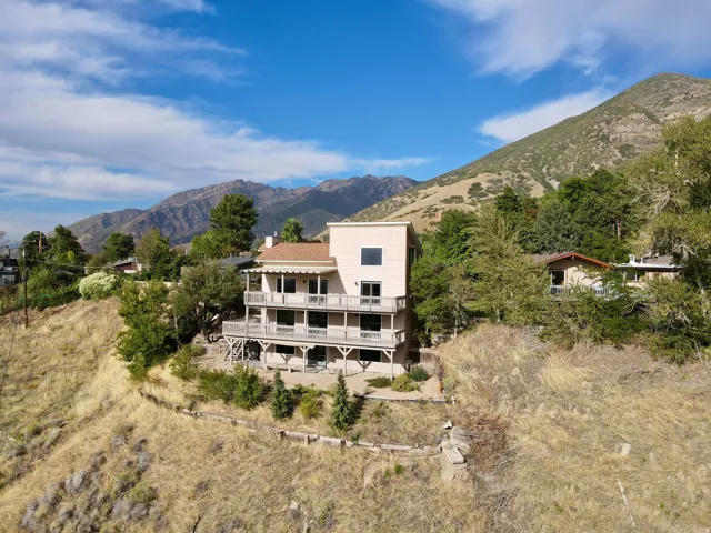 Multi-level dwelling with multiple balconies, a light-colored stucco exterior, and a prominent mountain backdrop