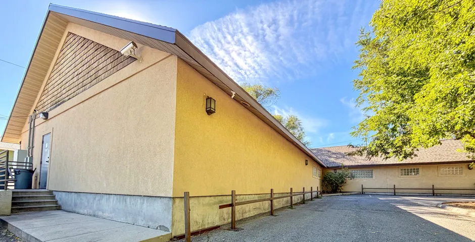 Stucco exterior with a peaked roofline, concrete walkway, and a paved parking area