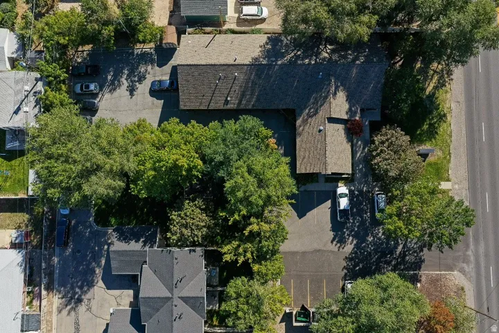 Paved parking lot, mature trees, adjacent street, and multiple buildings